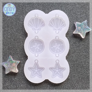 May include: A white silicone mold with six different shapes: two seashells, two sand dollars, and two starfish. The mold is designed for making resin earrings or other small crafts.