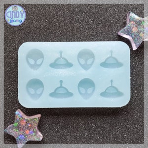 May include: A light blue silicone mold with six cavities. Each cavity is shaped like an alien head and a flying saucer. The mold is perfect for making resin crafts.