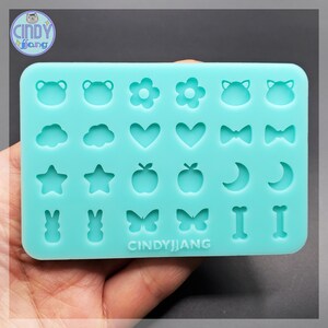 May include: A light teal silicone mold with various shapes, including flowers, hearts, stars, and butterflies. The mold also features the text "CINDY JANG".