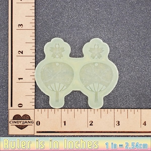 May include: A pair of clear resin earrings with a floral design and a fan-shaped design. The earrings are approximately 1 inch in diameter.