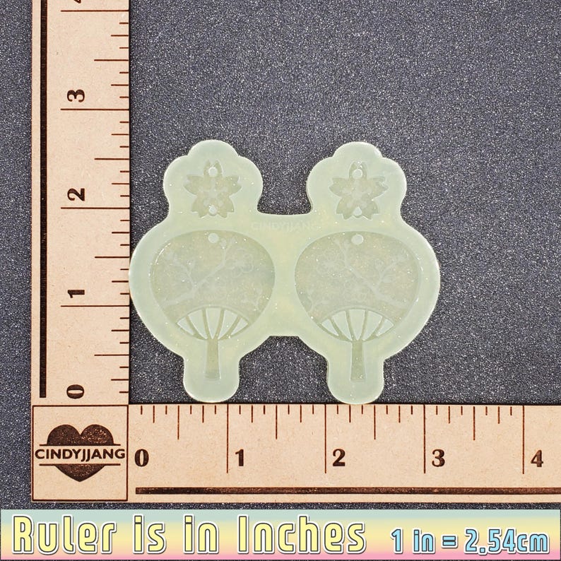 May include: A pair of clear resin earrings with a floral design and a fan-shaped design. The earrings are approximately 1 inch in diameter.