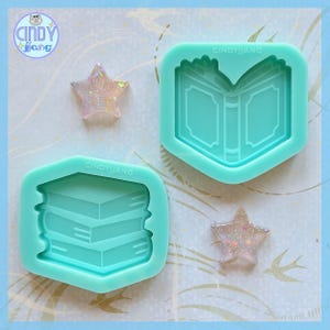 Puede incluir: Dos moldes de silicona color turquesa, uno con forma de pila de libros y otro con forma de libro abierto. También hay dos piezas de resina con forma de estrella brillante. Los moldes tienen el texto "CINDYJIANG".