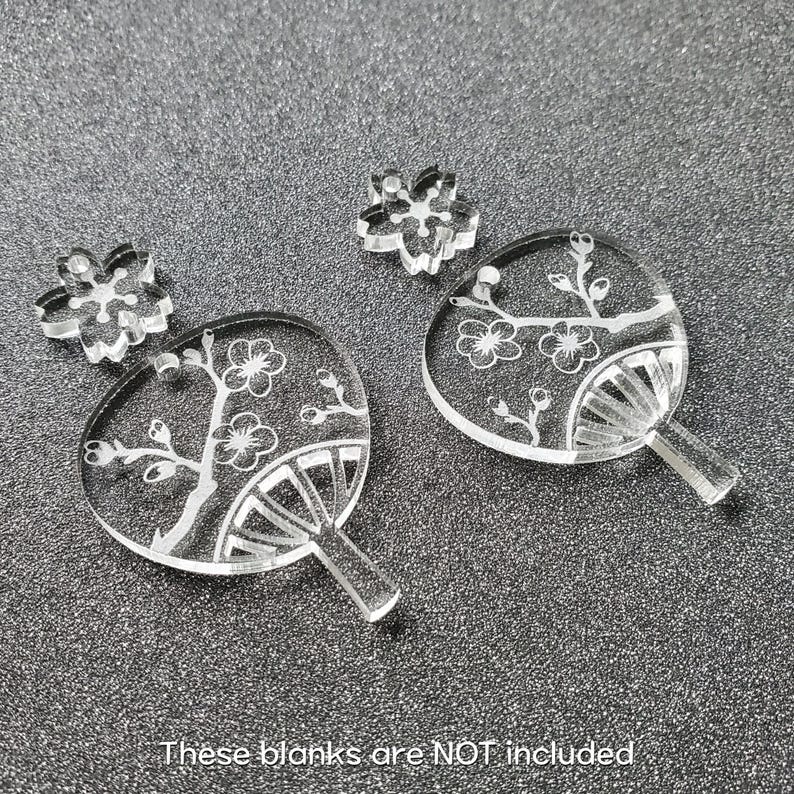May include: Four clear acrylic earrings with a floral design. The earrings are shaped like fans and feature a delicate floral pattern.