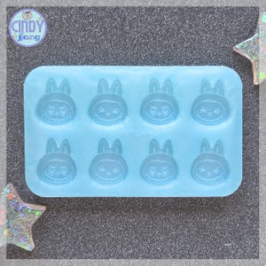 May include: A light blue silicone mold featuring eight bunny-shaped cavities. Each bunny has a unique expression, with details like eyes, mouths, and ears. The mold is designed for crafting and includes the text "CINDY JANG".