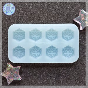 May include: A clear silicone mold with six impressions of a 20-sided die, each with a different symbol. The symbols are a crescent moon and a star.