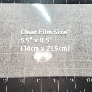 May include: A clear film sheet on a black grid surface. The film is 5.5 inches by 8.5 inches, or 14 centimeters by 21.5 centimeters.