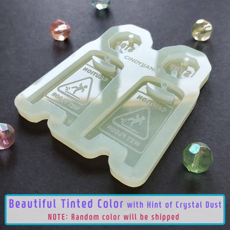 May include: A clear silicone mold for making resin earrings. The mold features two wet floor signs with the text "Caution Wet Floor" and a stick figure slipping on the wet floor. The mold is translucent and has a hint of glitter.