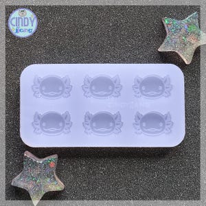 Könnte beinhalten: Eine Silikonform mit sechs Axolotl-Formen. Die Form ist helllila und hat eine glatte Oberfläche.