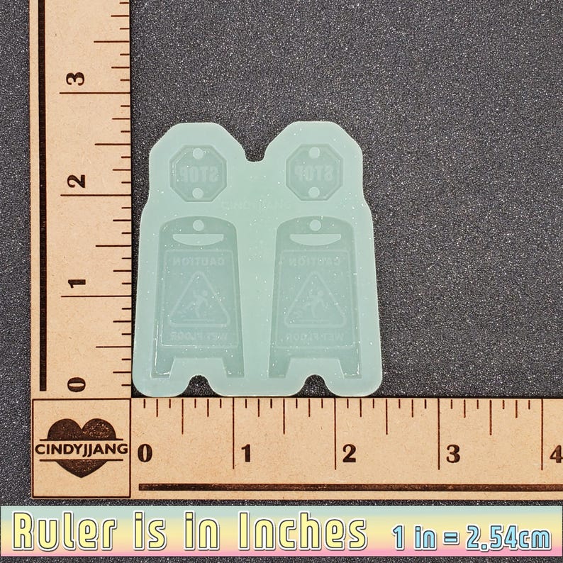 May include: Two clear silicone molds for making resin crafts. Each mold is shaped like a caution sign with the words "Caution" and "Slippery When Wet" in a black font. The molds are 1.5 inches tall and 1 inch wide.