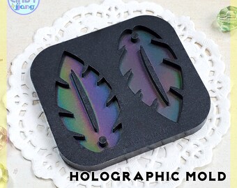 May include: A black silicone mold with two feather shapes. The mold is holographic and has a rainbow iridescent sheen.