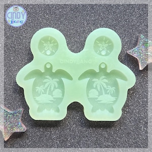 May include: A light green silicone mold featuring two turtle shapes with palm tree and sunset designs, and two sand dollar shapes. The mold has the text "CINDY JIANG" and "CINDY fang".