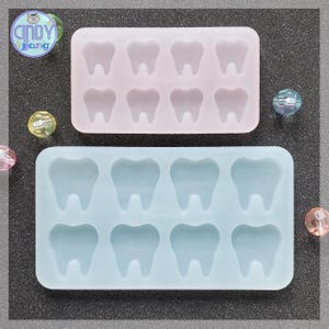 May include: Two silicone molds for making resin crafts. The top mold is pink and has 6 tooth shapes. The bottom mold is blue and has 8 tooth shapes.