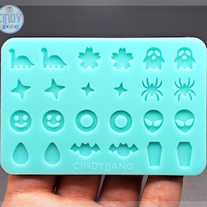 May include: A turquoise silicone mould with 18 different shapes for crafting. The shapes include dinosaurs, stars, smiley faces, rings, aliens, bats, teardrops, and coffins. The mould is labelled "CINDYJJIANG".