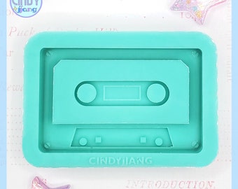 May include: A teal blue silicone mold shaped like a cassette tape. The mold has a raised design of a cassette tape with the words "CINDYJJANG" at the bottom.