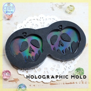 May include: A black silicone mold for making resin crafts. The mold is shaped like two poison apples with a skull design and iridescent holographic finish. The mold is labeled "HOLOGRAPHIC MOLD" and "CINDYJIANG".