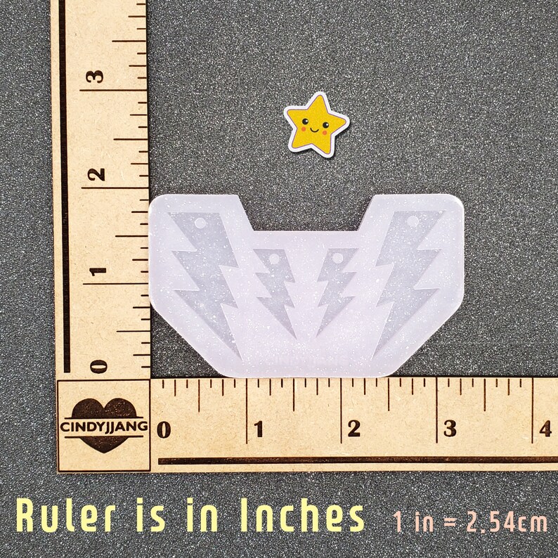 K&ouml;nnte beinhalten: Eine transparente Silikonform mit drei Blitzformen. Die Form ist etwa 5 cm breit und 4 cm hoch. Die Form befindet sich auf einem Holzlineal mit Zollmarkierungen.