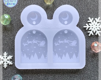 May include: A clear silicone mold in a frog shape with two arched sections featuring a winter scene with Santa's sleigh and trees. The mold has the text "CINDYJANG" and "CINDY fang". Decorative crystals and snowflakes surround the mold.
