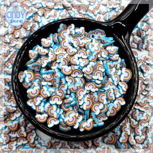May include: A black bowl filled with rainbow-colored sprinkles. The sprinkles are shaped like rainbows with white clouds. The bowl is sitting on a white surface.