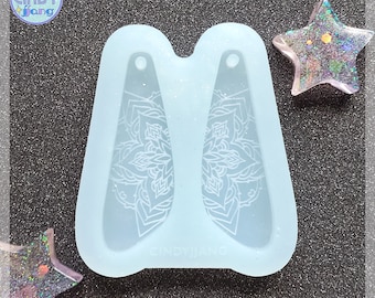 May include: A light blue silicone mold for making earrings. The mold has two cavities, each shaped like a teardrop with a mandala design. The mold is labeled "Cindy Jang".