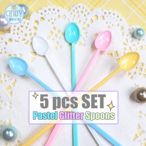 May include: A set of five pastel-colored glitter spoons in blue, white, teal, pink, and yellow. The spoons are arranged on a white lace doily. Text on the image reads "5 pcs SET Pastel Glitter Spoons."
