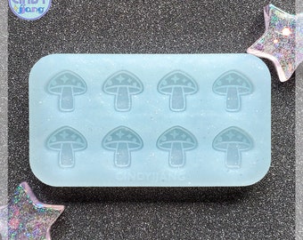 May include: A light blue silicone mold with eight mushroom-shaped cavities. Each mushroom has a white star design on the top.