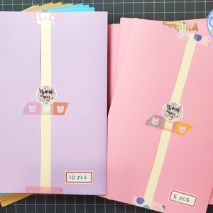 May include: Two stacks of colored cardstock paper, one pink and one purple, with a thank you sticker on each stack. The pink stack has 5 pieces and the purple stack has 10 pieces.