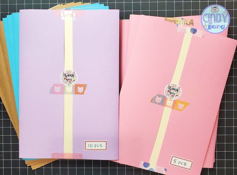 May include: Two stacks of colored cardstock paper, one pink and one purple, with a thank you sticker on each stack. The pink stack has 5 pieces and the purple stack has 10 pieces.