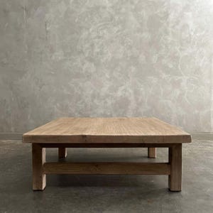 May include: A large, rectangular wooden coffee table with a natural finish. The table has a thick top and sturdy legs, showcasing a rustic design. The table is approximately 48 inches long, 30 inches wide, and 16 inches high.