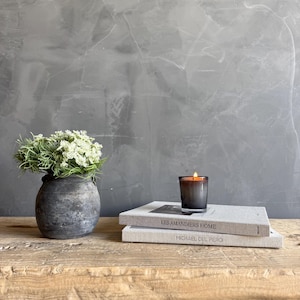 May include: A white ceramic mug with a black handle and the text "But First, Coffee" in a bold, black font. The mug is filled with a dark liquid, likely coffee, and sits on a light-colored surface.