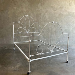 May include: White metal bed frame with a decorative, ornate headboard and footboard. The frame has a simple, rectangular design with rounded corners and decorative accents.