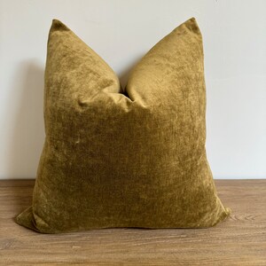 May include: A soft, plush pillow with a deep green velvet cover. The pillow is square and has a simple, elegant design.