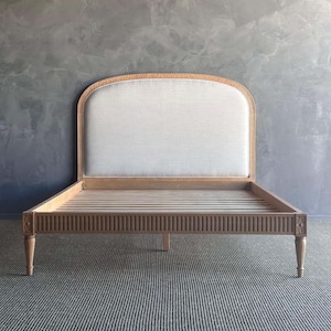 May include: A wooden bed frame with a curved headboard and a light gray upholstered headboard. The bed frame has a slatted base and carved details.