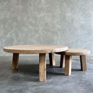 May include: Two round wooden coffee tables with four short legs each. The larger table is in front of the smaller table.