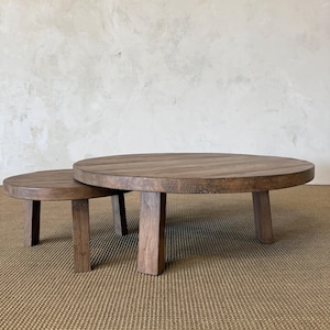 May include: A set of two round wooden coffee tables with a dark brown finish. The tables feature thick, circular tabletops supported by four sturdy, straight legs each. The smaller table is partially tucked underneath the larger table.