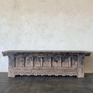 May include: A long, rectangular wooden console table with a weathered, dark brown and black finish. The front features six cabinet doors adorned with intricate, carved lattice patterns and a decorative geometric border along the bottom edge.