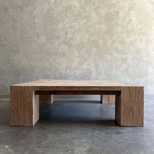 May include: A large, rectangular coffee table made of light-colored wood with a thick, solid top and four chunky legs. The table has a rustic, weathered look.