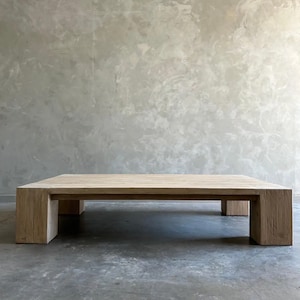 May include: A large, rectangular, light wood coffee table with a simple design. The table has a thick top and four square legs.