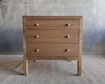 May include: A three-drawer dresser made of wood with a light brown finish. The dresser has brass knobs and sits on four legs.