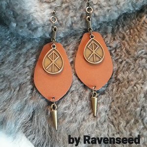 May include: A pair of orange leather earrings with a bronze pendant featuring a Viking symbol. The earrings have a pointed bronze tip at the bottom.