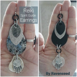 May include: Reiki Spirit Guide Earrings with a black and white layered teardrop design and a silver charm with a spiral and hand symbol. By Ravenseed.