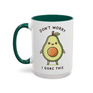 Puede incluir: Taza de café de cerámica blanca con un borde verde. La taza presenta un aguacate de dibujos animados con una cara sonriente y el texto "Don't Worry I Guac This".
