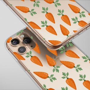Puede incluir: Dos fundas transparentes para teléfono con un patrón repetido de zanahorias naranjas con copas verdes. Las fundas están sobre un fondo claro. Las fundas del teléfono tienen un marco de color dorado.