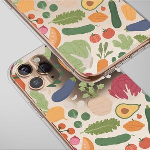 Puede incluir: Dos fundas transparentes para teléfono con un colorido diseño de verduras. El diseño incluye ilustraciones de tomates, pepinos, berenjenas, aguacates y lechuga. Las fundas tienen un borde dorado y se muestran sobre un fondo gris claro.