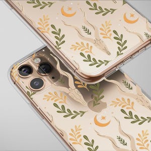 May include: Two clear phone cases with a repeating pattern of beige antelope skulls, green and yellow leaves, and crescent moons. The cases are made of clear plastic and have a gold-colored trim.