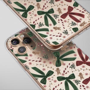 May include: Two clear phone cases with a festive Christmas pattern. The design includes green and burgundy bows, gingerbread men, candy canes, and snowflakes on a cream background. The cases have a gold-colored frame.