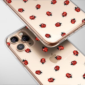 May include: Two clear phone cases with a repeating pattern of red ladybugs with black spots and antennae. The cases are on a light background, showcasing the design and the phone's features.