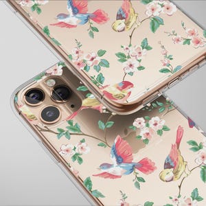 Op de afbeelding: Twee transparante telefoonhoesjes met een bloemen- en vogelontwerp. De hoesjes hebben een patroon van roze bloemen, groene bladeren en kleurrijke vogels tegen een beige achtergrond. De hoesjes zijn gemaakt van transparant materiaal.