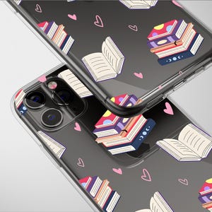 May include: Transparent phone case featuring a pattern of colourful stacked books, open books, and pink hearts on a dark grey backdrop. The case is designed for a smartphone, with camera and button cutouts visible.