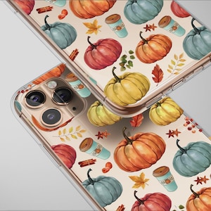 May include: Clear phone cases with a fall-themed pattern. The design features watercolor pumpkins in shades of orange, red, and yellow, along with blue pumpkins, coffee cups, and autumn leaves. The cases are angled, showcasing the camera lenses.