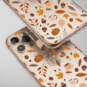 May include: Two clear phone cases with a fall-themed pattern. The design includes pumpkins, leaves, acorns, coffee cups, and coffee beans in shades of brown, orange, and beige. The cases are slightly overlapping.